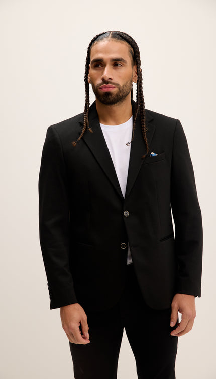 Man wearing a black suit with a white shirt on a plain background