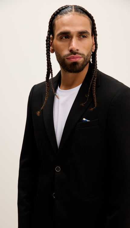 Man wearing a black blazer over a white shirt against a plain background