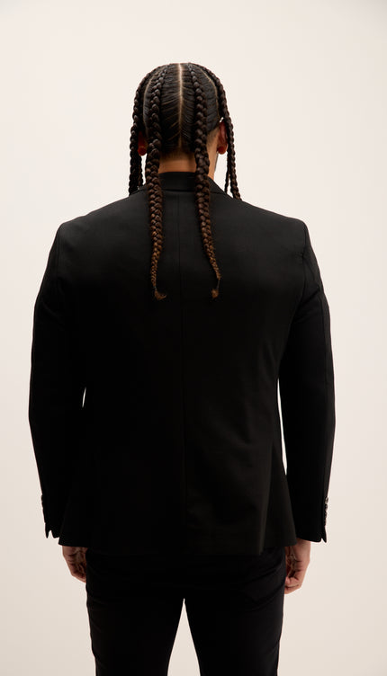 Person wearing a black suit with braided hair on a plain background