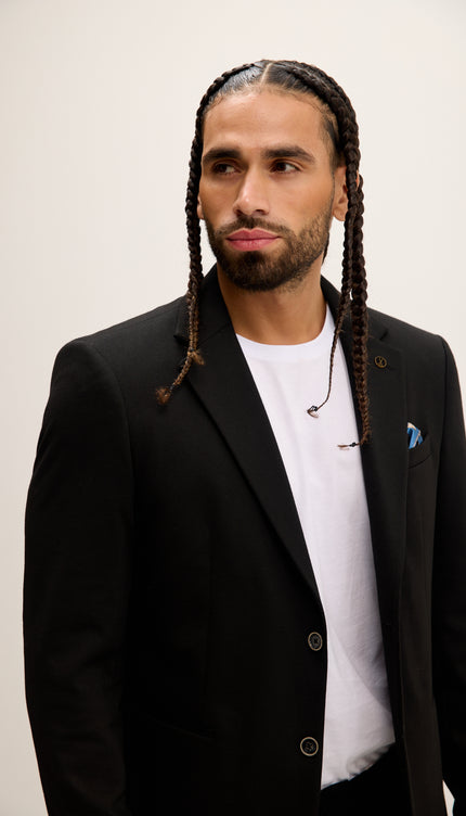 Man wearing a black blazer over a white shirt with a plain background