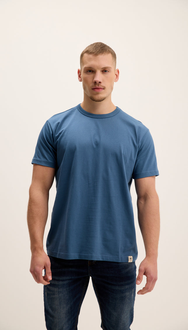 Man wearing a blue t-shirt and jeans on a plain background