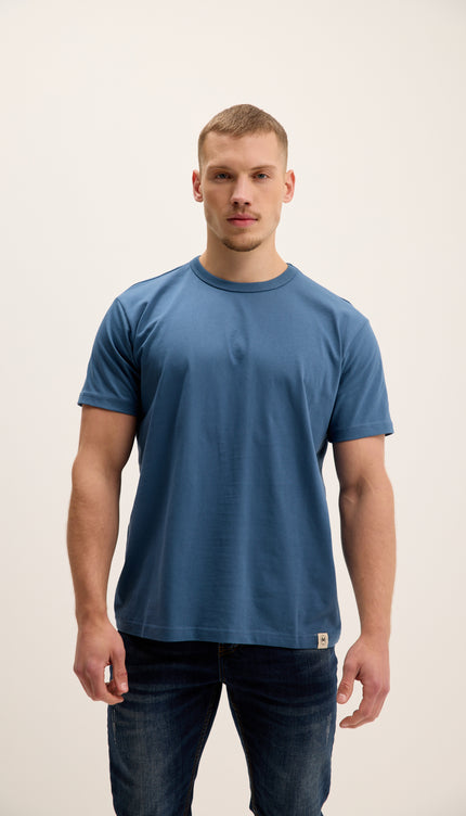 Man wearing a blue t-shirt and jeans on a plain background