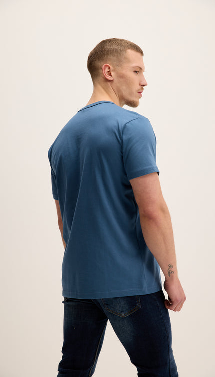 Man wearing a blue t-shirt and dark jeans on a plain background