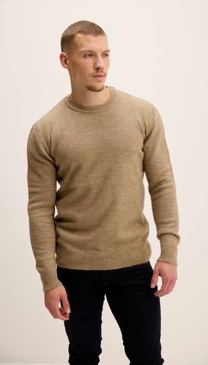 Man wearing a beige sweater and dark pants on a white background