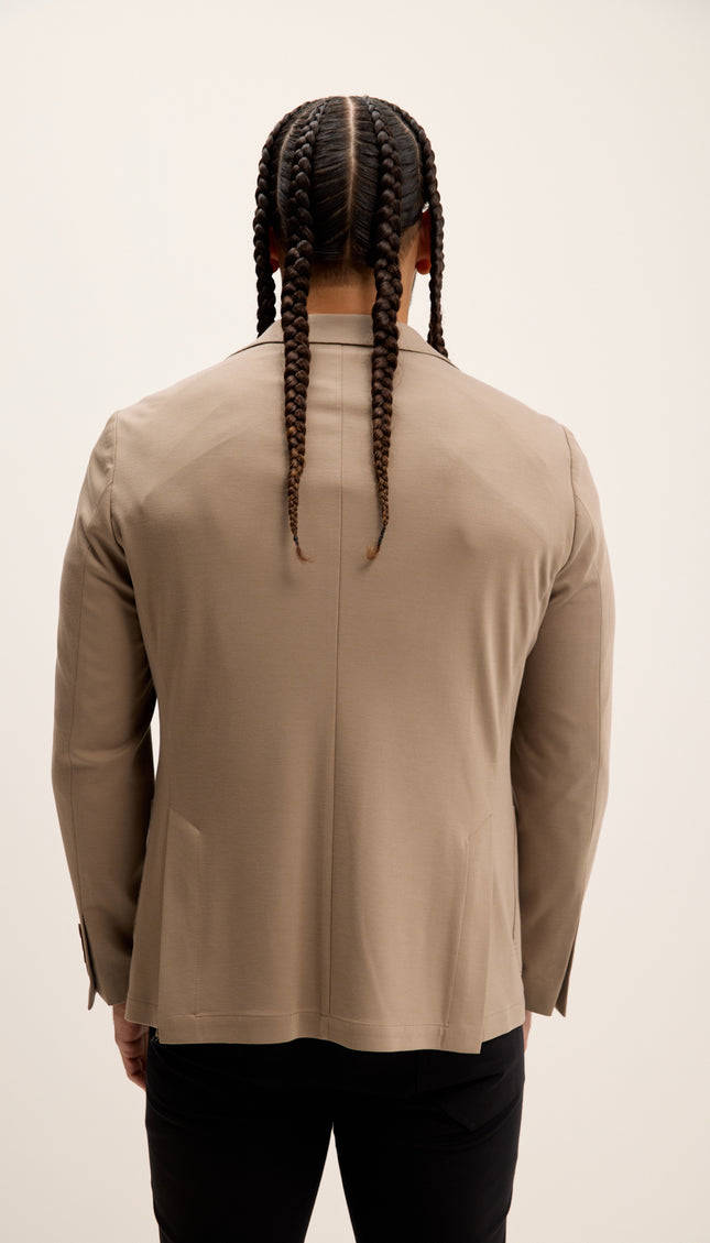 Person wearing a beige jacket with braided hair on a plain background