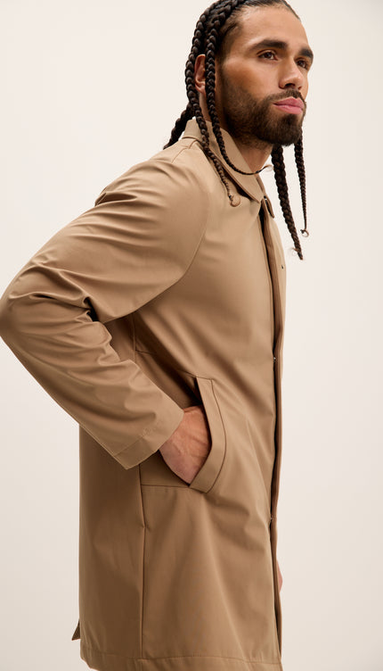 Man wearing a beige trench coat against a plain background