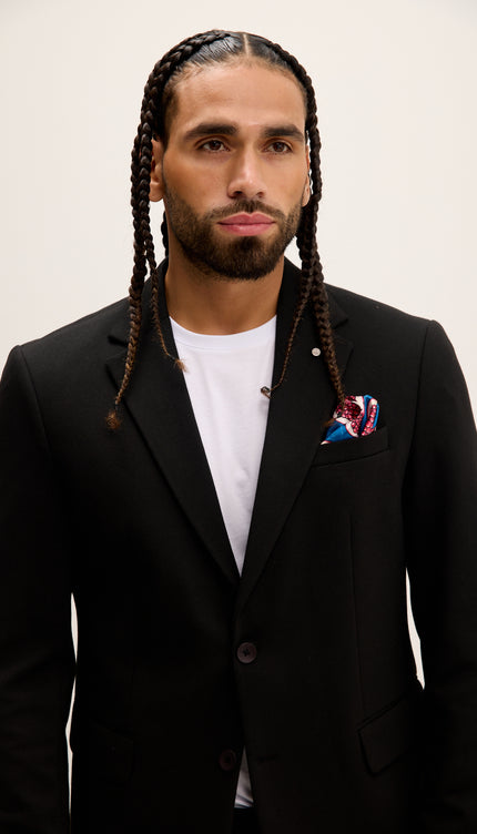Man wearing a black suit with a white shirt and colorful pocket square on a plain background