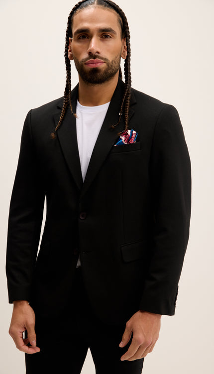 Man wearing a black suit with a white shirt and colorful pocket square on a plain background