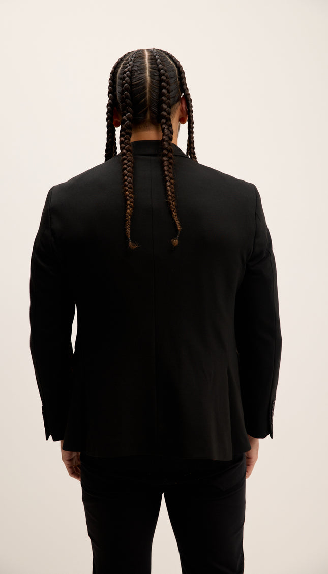 Person wearing a black suit with braided hair on a plain background