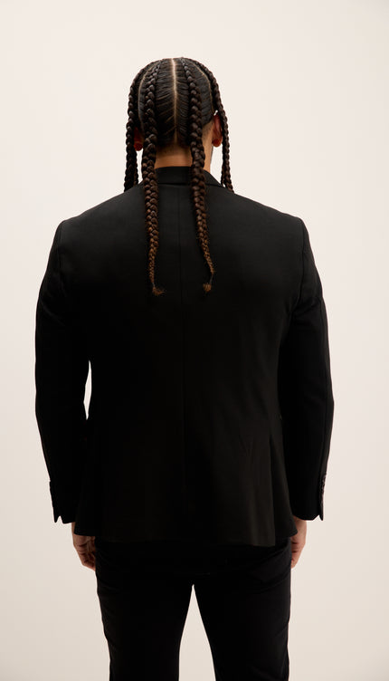 Person wearing a black suit with braided hair on a plain background