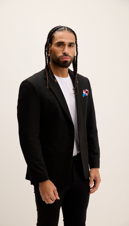 Man wearing a black suit with a white shirt and colorful pin on a plain background