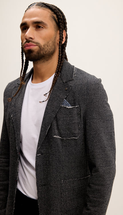 Man wearing a dark gray blazer over a white shirt with a plain background