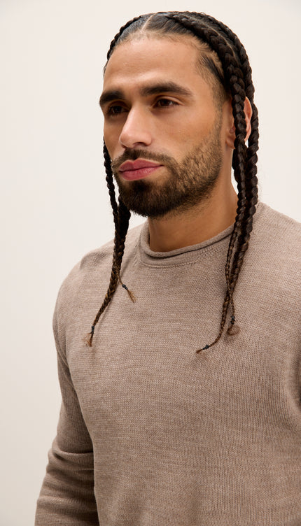 Man with braided hair wearing a beige sweater against a plain background