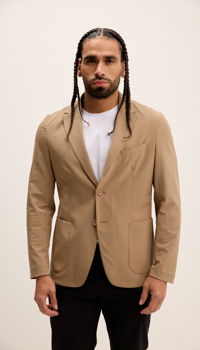 Man wearing a beige blazer over a white shirt with a plain background
