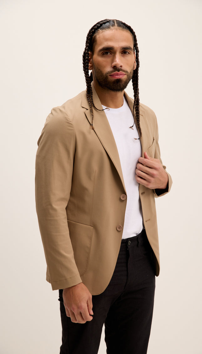 Man wearing a beige blazer over a white shirt with a plain background