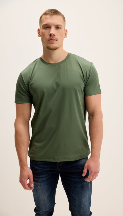 Man wearing a green t-shirt and blue jeans against a plain background