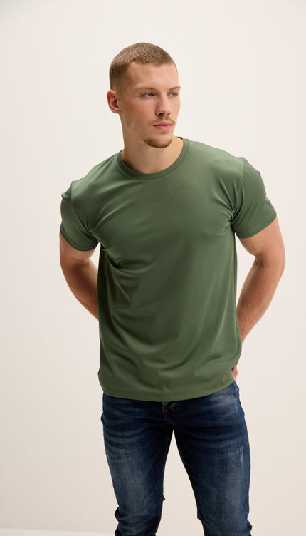 Man wearing a green t-shirt and blue jeans against a plain background