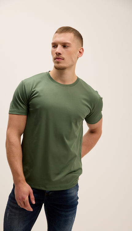 Man wearing a green t-shirt and blue jeans against a plain background