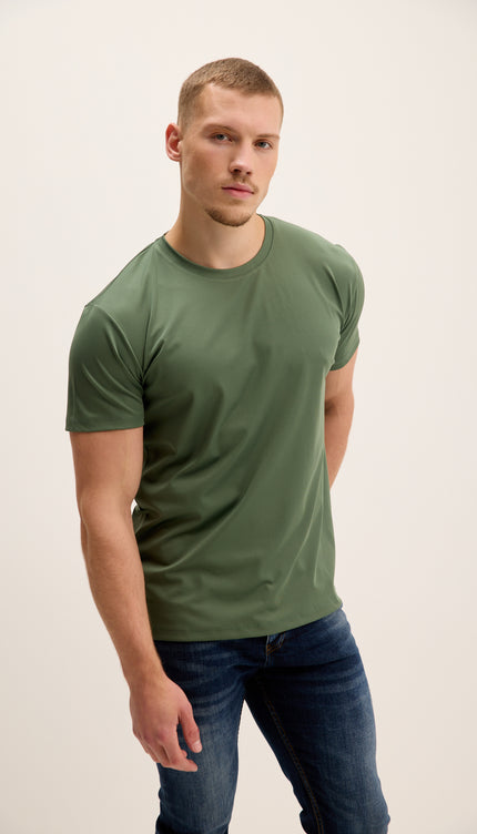 Man wearing a green t-shirt and blue jeans against a plain background