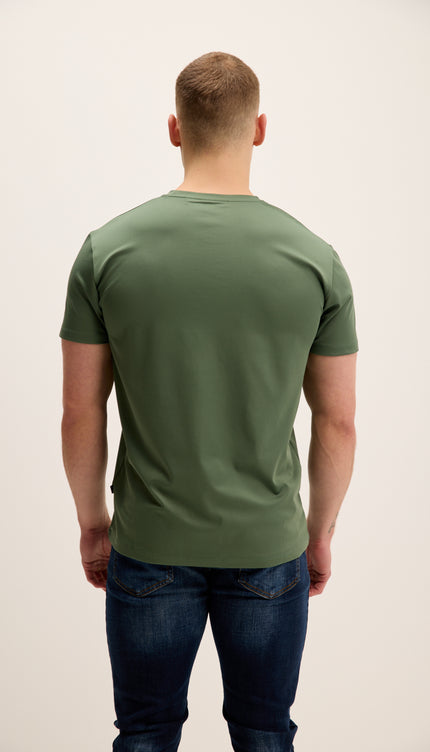 Man wearing a green t-shirt and blue jeans against a plain background