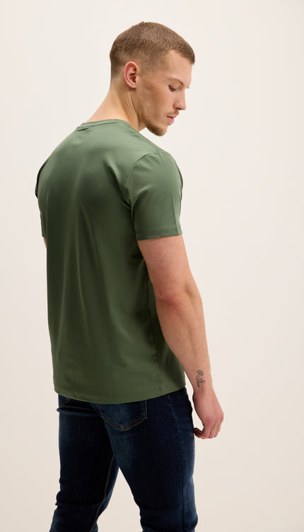 Man wearing a green t-shirt and dark jeans on a plain background