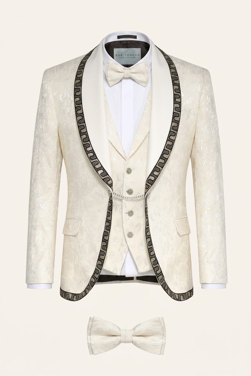 Cream floral brocade shawl lapel tuxedo suit with intricate decorative trim, matching vest, and bow tie for mens formal wear.